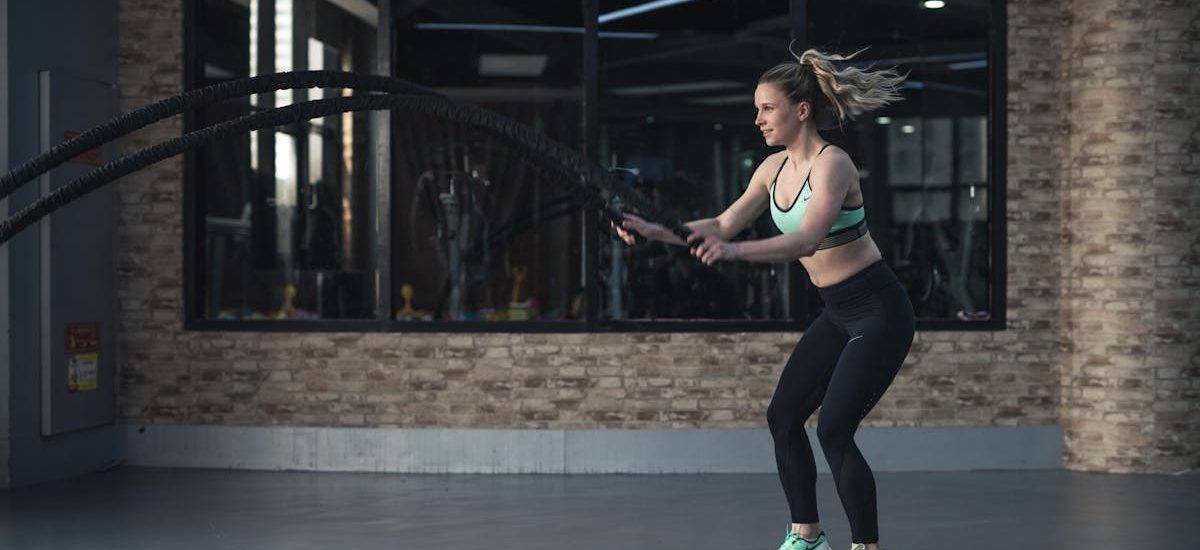 Focused woman performing CrossFit rope training indoors, demonstrating strength and endurance.